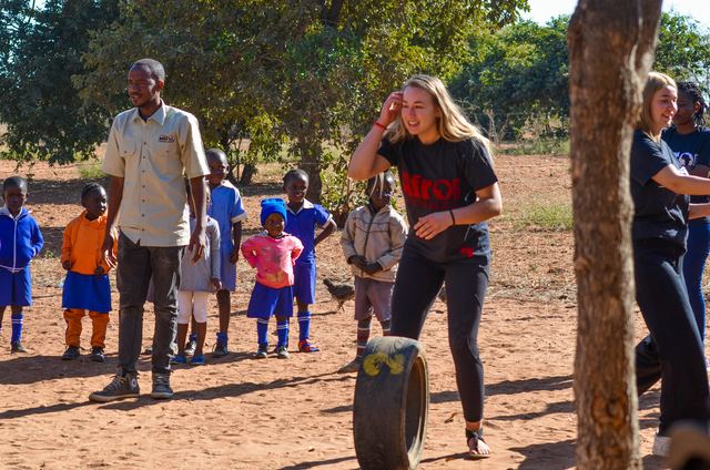 A volunteer and a local staff member with children in school uniform beside a rolling tyre