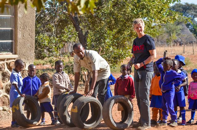 Children in school uniform standing in a line with tyres next to a volunteer and a teacher
