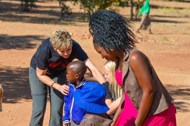 A volunteer bending down to greet a child while others look on