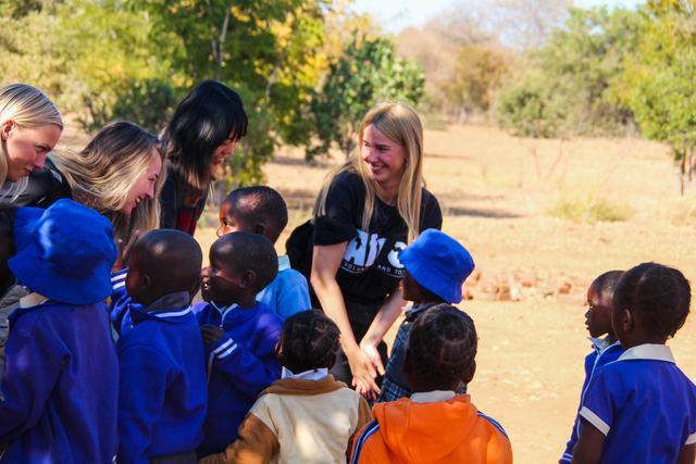 A volunteer smiling among children in blue uniforms and hats