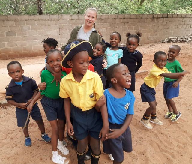 Children and a volunteer posing together in a sandy playground