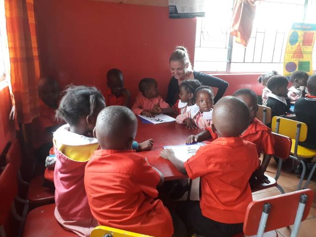 A volunteer drawing with young children at a table in a bright red classroom