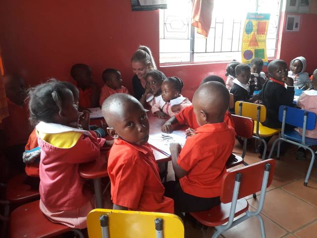Young children sitting at tables in a red classroom doing drawing work