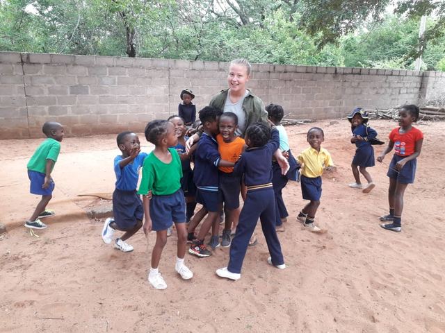 Children and a volunteer gathered in a sandy school yard