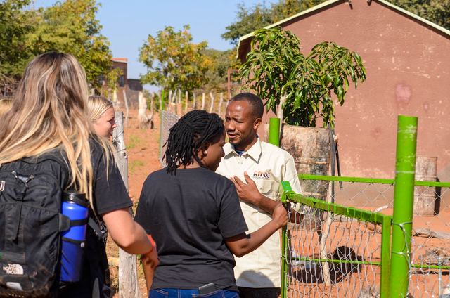 Volunteers speaking with a community guide next to a fence with green posts