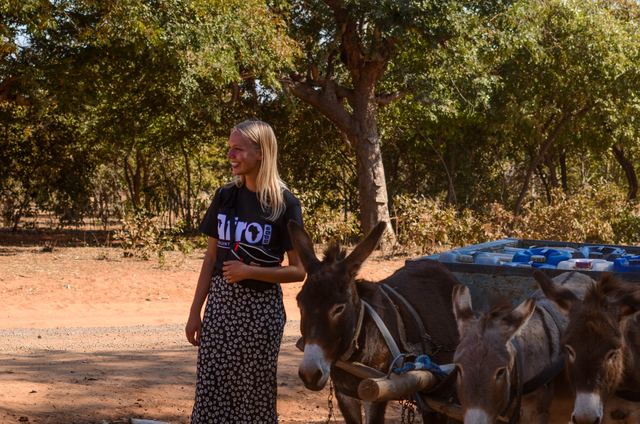 A volunteer standing beside donkeys that haul water in a village