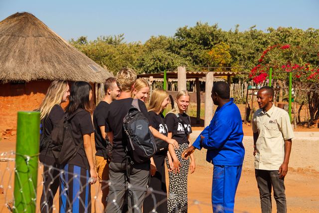 Volunteers meeting a man in blue overalls next to a fence with green posts