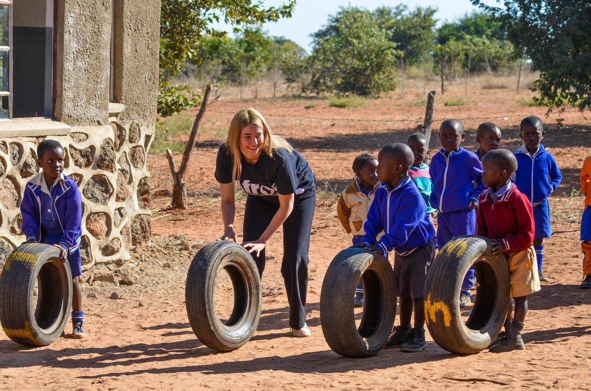 Volunteers rolling tyres in a play game with children on red earth