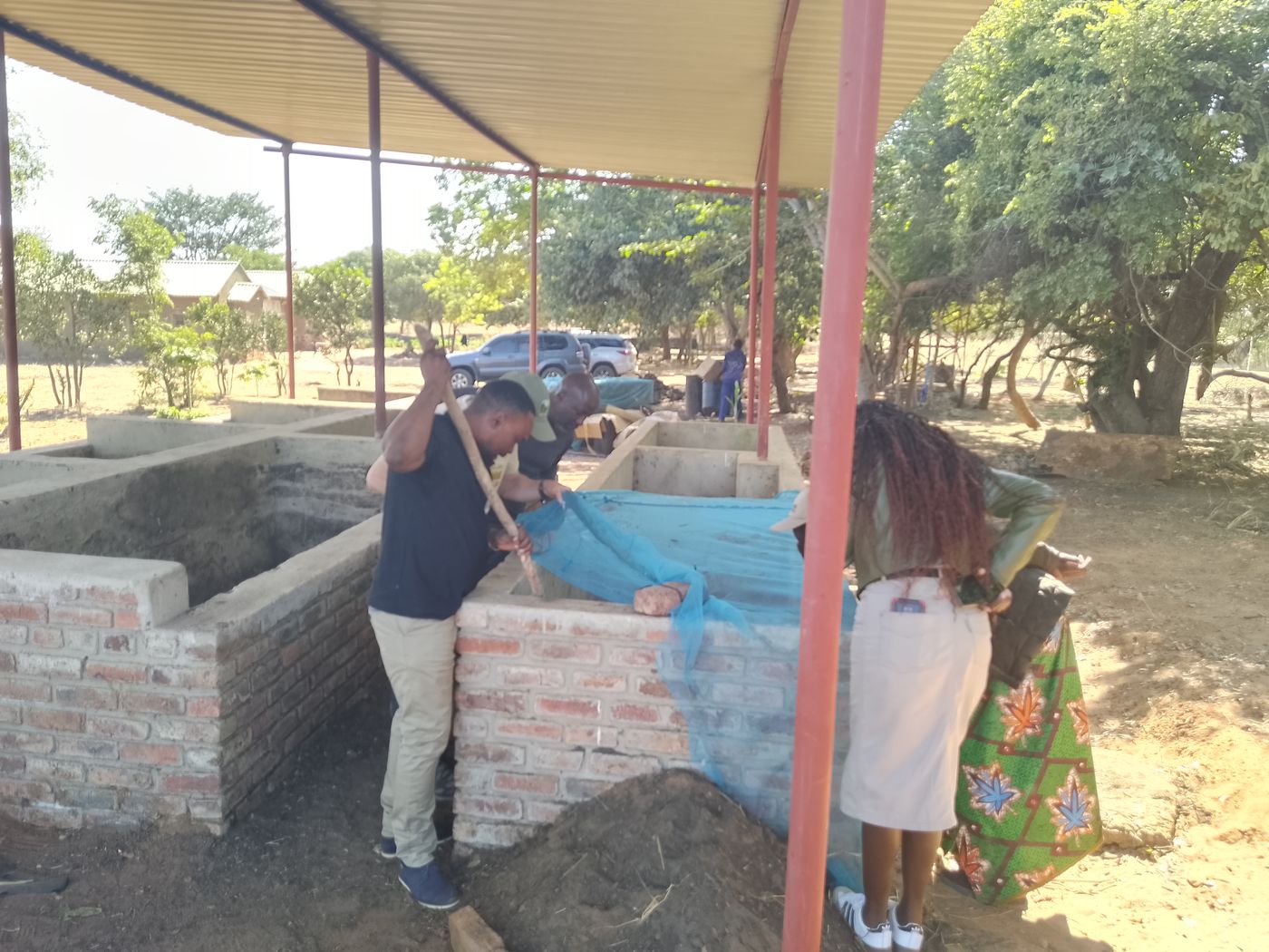 Two people working at a brick compost bay under a roofed shelter